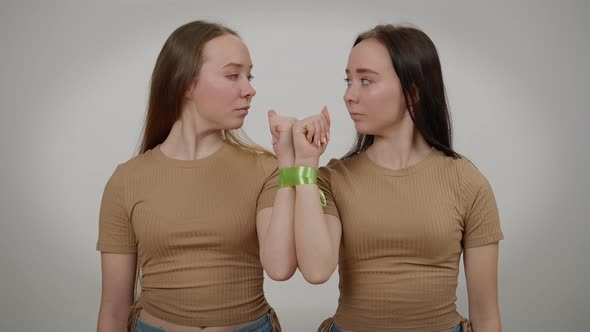 Twins with Serious Facial Expression Posing at Grey Background with Tied Hands alt