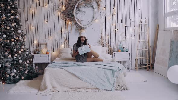 Wide Angle in Which a Beautiful Girl Sitting on the Bed Opens a Gift. alt