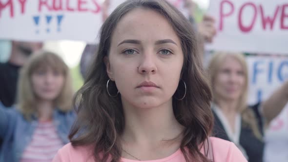 Close-up Portrait of Young Beautiful Woman Closing Mouth with Hands As Crowd of People Protesting at alt