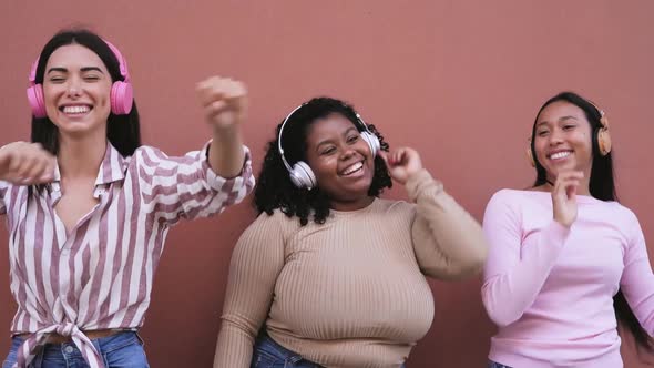 Happy young women having fun dancing and listening music with wireless headphones alt