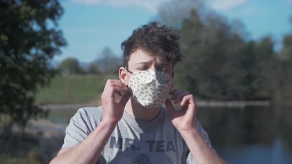 Young man puts on homemade white corona virus cotton mask MEDIUM SHOT alt