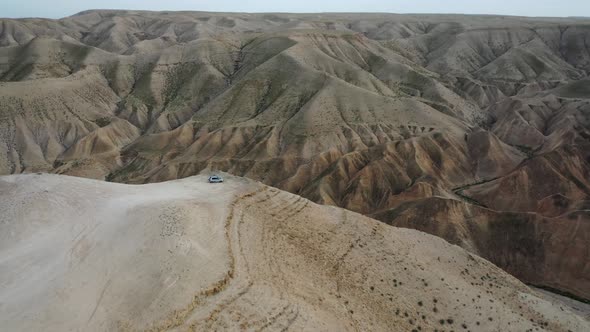 breathtaking tilt down on a car standing at a cliff, Judean desert, Israel, aerial shot alt