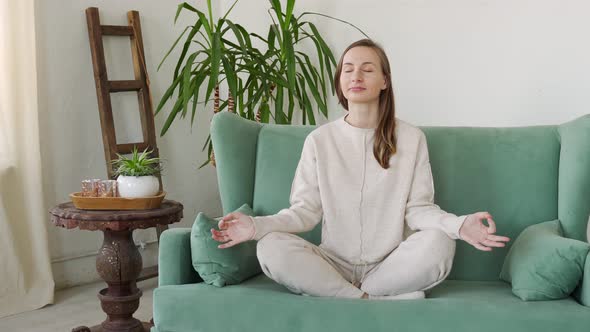 Young Woman Sit on Couch in Living Room Practice Yoga Relieve Negative Emotions at Home alt