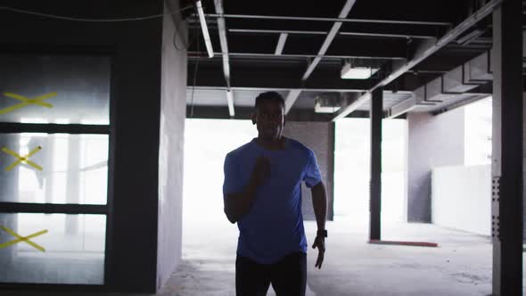 African american man wearing sports clothing jogging through an empty urban building alt
