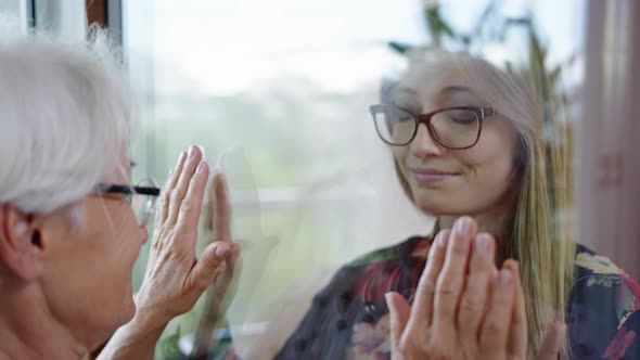 Young Lady in Quarantine Speaking with Her Grandmother Through the Glass Window. Protecting alt