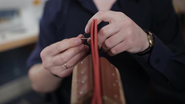 Man Creates a Brown Leather Wallet with His Own Hands with a Needle in the Leather Workshop Closeup
