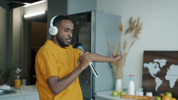 Playful Young Man Singing in Microphone Listening to Music Through Headphones and Playing Guitar in alt