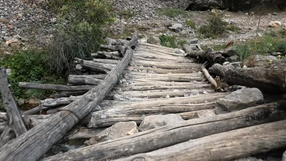 An old wooden footbridge over a mountain river. The camera moves over the bridge.