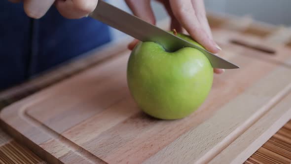Closeup woman hands cutting apple on wooden board in kitchen.