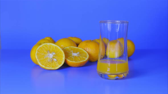 Stop motion shot, orange juice level increasing, and oranges on blue background.