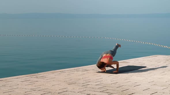 fit woman practices yoga on stone paving with sea and sky on background alt