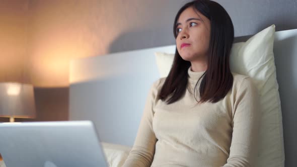 Young woman sitting on bed using laptop for work in bedroom at home