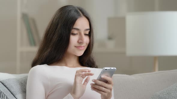 Female Young User Freelancer Calm Attractive Girl Arab Hispanic Woman Sits on Sofa at Home Scrolls alt