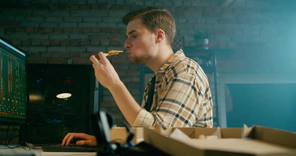 Coder Works at PC Eating Pizza in Loft Electronics Workshop or Home Garage