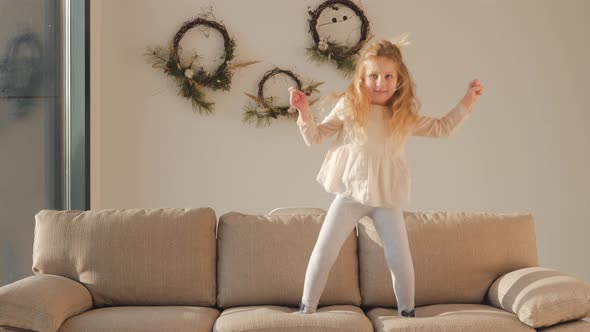 happy little girl jumping on sofa dancing having fun child in playful mood enjoying weekend morning