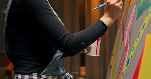 A Student in Denim Dungarees in Art Class Paints an Abstract Modern Picture with Red alt