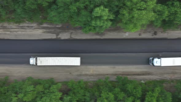 Aerial Shot of White Trucks Driving on New Freeway Running Through Forest alt