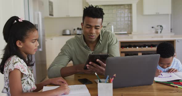 African american father, daugher and son sitting at kitchen table doing homework alt