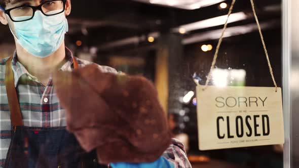 Business owner attractive young man in apron hanging we're open sign alt