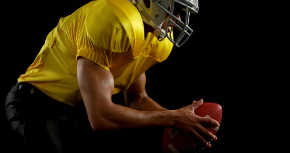 American football player bending holding a ball on turf with both his hands alt