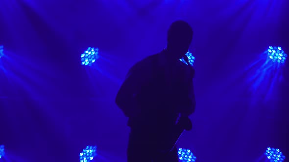 Silhouette a Young Retro Stylish Guy Plays on the Golden Shiny Saxophone in the Blue Spotlights on alt