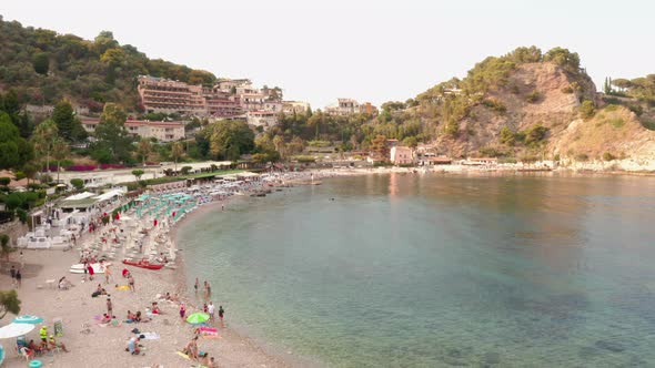 Bird's eye view of a crowded sandy beach by the clear Mediterranean Sea. Taormina, Sicily, southern alt