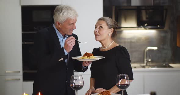 Senior Handsome Man Feeding Attractive Wife with Pasta Celebrating Anniversary Together at Home alt