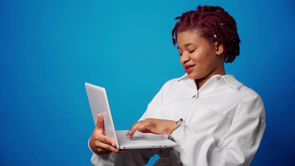 Young Afro Woman Holding Laptop and Typing Against Blue Background