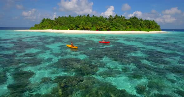 Aerial drone view of a man and woman couple kayaking around a tropical island alt