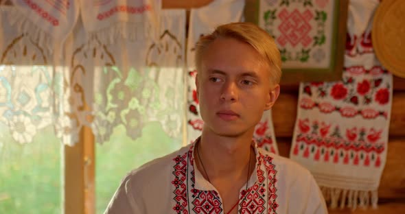 Portrait of a Handsome Young Man of Slavic Appearance in a Folk Costume Sits in a Russian Hut By the alt