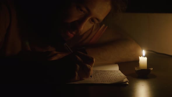 Closeup of Man Writing By Pen in Candlelight at Darken Room
