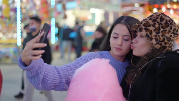 Two Female Best Friends Take Pictures Together at the Funfair at Night Holding Cotton Candy and alt