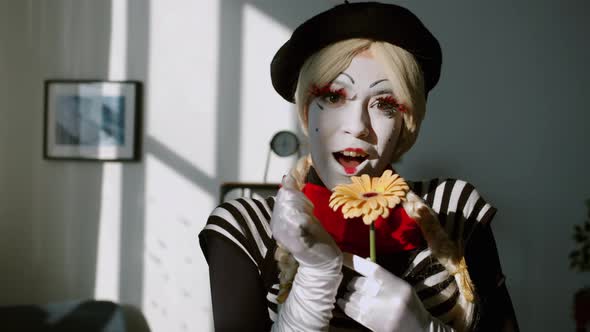 Portrait of Pretty Girl Mime Smelling Flower and Smiling Looking at Camera at Home alt