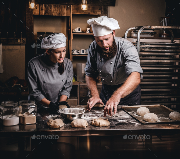 Chef teaching his assistant to bake the bread in a bakery.