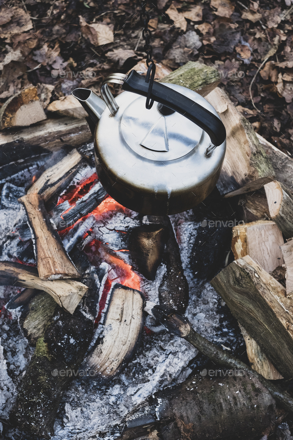 Metal tea kettle heating up over a campfire stock photo - OFFSET