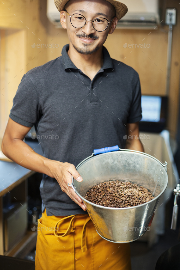 Japanese man wearing hat and glasses standing in an Eco Cafe, holding metal bucket with freshly - Stock Photo - Images