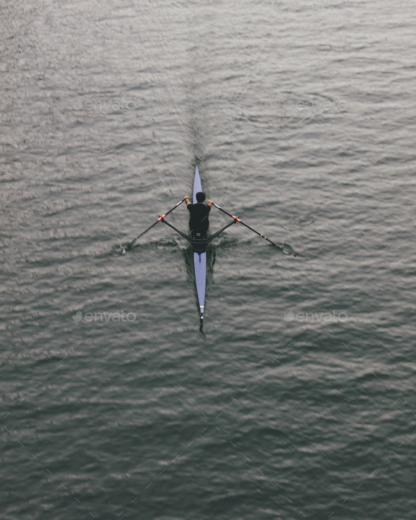 Overhead view of an oarsman in a single scull boat on calm water mid stroke, motion blur.