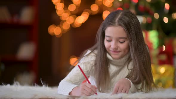girl writes a letter to Santa Claus against the background of a festive Christmas tree