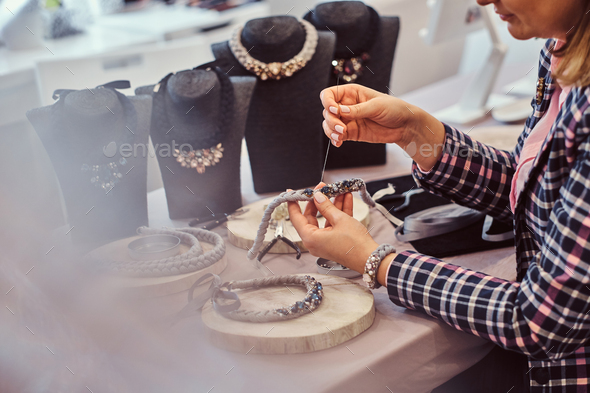 Elegantly dressed woman makes handmade necklaces in jewelry workshop.