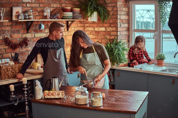 Mom dad and little daughter together cooking breakfast in loft style kitchen.