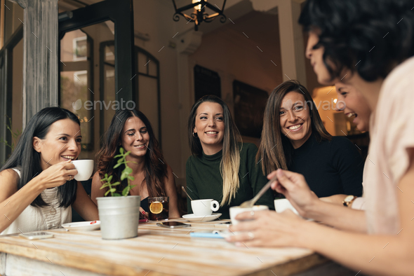 Six beautiful women drinking coffee and chatting. Stock Photo by nunezimage