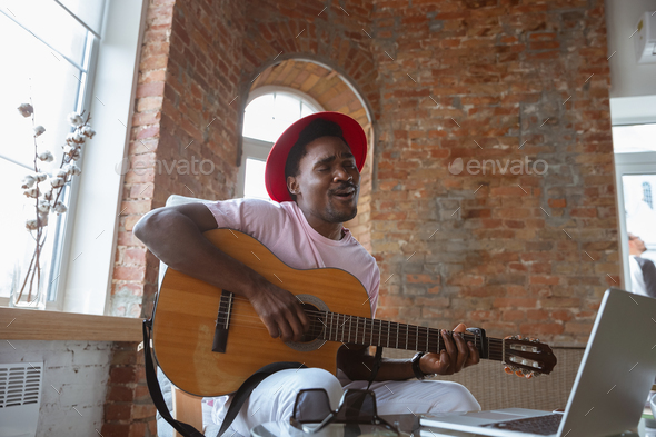 African-american musician playing guitar during online concert at home isolated and quarantined