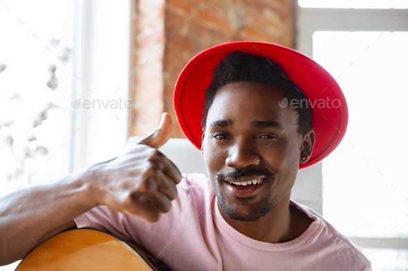 African-american musician in red hat greeting audience before online concert at home isolated and