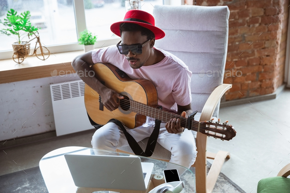African-american musician playing guitar during online concert at home isolated and quarantined