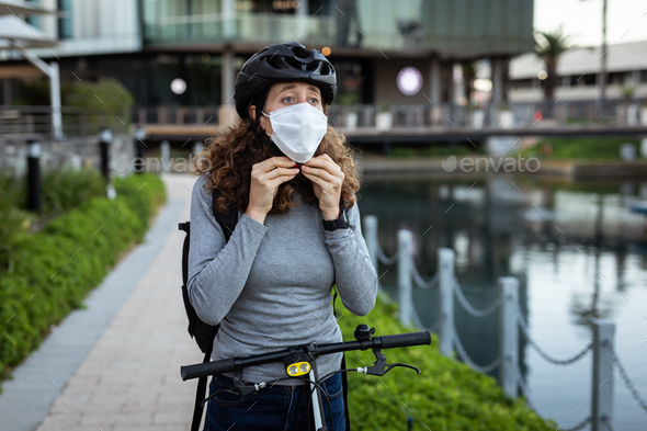 Caucasian woman putting on a protective mask and wearing a cycling helmet in the streets