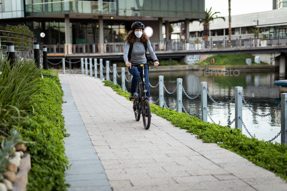 Caucasian woman wearing a protective mask and a cycling helmet in the streets, biking in the streets