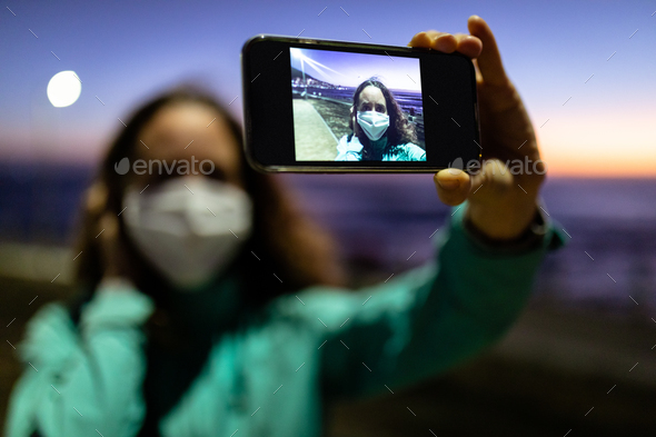 Caucasian woman wearing a protective mask against coronavirus, taking a picture in the streets