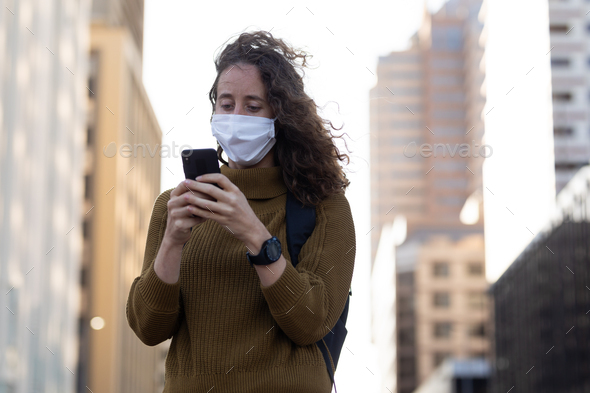 Caucasian woman wearing a protective mask and using her phone in the streets