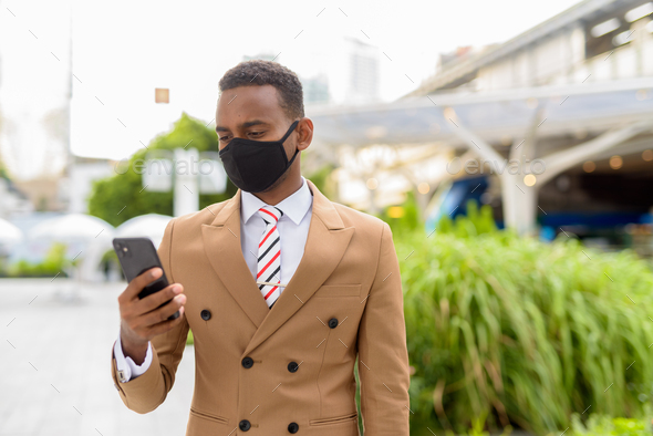 Young African businessman using phone with mask for protection from corona virus outbreak in the