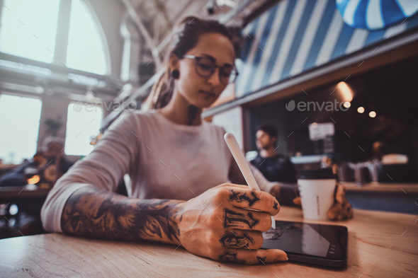 Tattooed girl in glasses is drawing in her digital pad - Stock Photo - Images